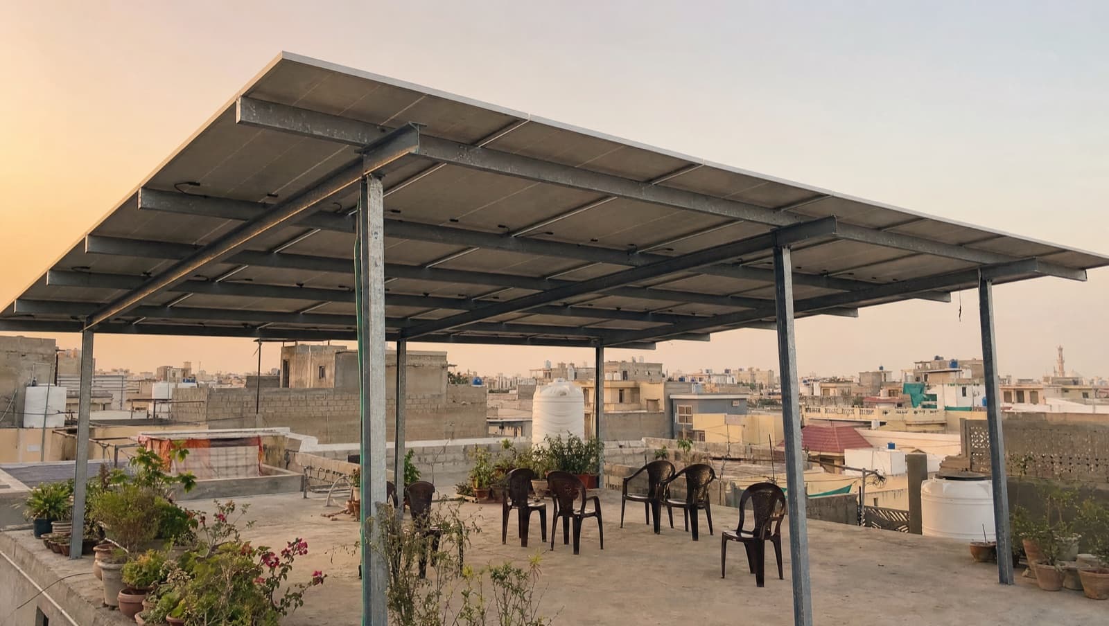 Solar panels raised on a galvanised steel frame above a flat Karachi rooftop with space underneath