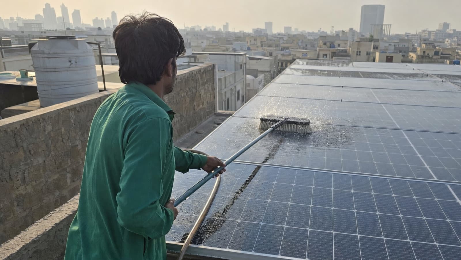 A technician cleaning rooftop solar panels with a soft brush and water in early morning light